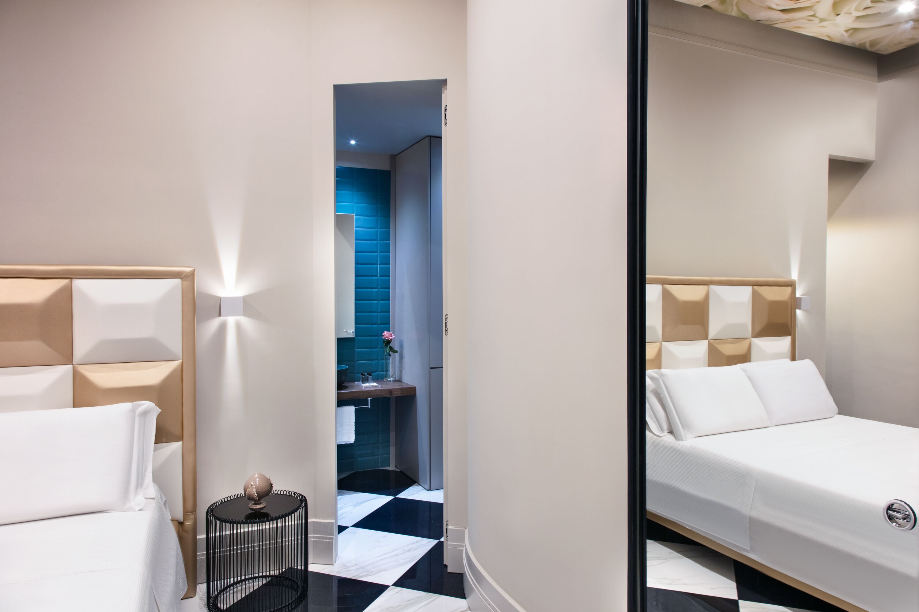Quarto de hotel moderno com uma cama, uma mesa redonda pequena e um banheiro visível através de uma porta aberta.