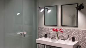 Ein modernes Badezimmer mit Duschkabine aus Glas, einem weißen Waschbecken mit Marmorablage und zwei wandmontierten Spiegeln mit Einbaustrahlern.
