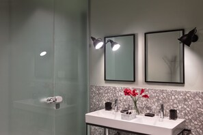 A modern bathroom with a glass shower enclosure, a white sink with a marble backsplash, and two wall-mounted mirrors with spotlights. - Lady Rose Privilege Suite (Naples)
