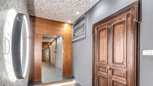 Un pasillo con una puerta de madera, un espejo y un papel tapiz estampado.