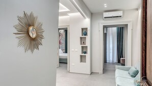 Una sala moderna con un sofá azul claro, una decoración de sol en la pared y un pasillo que lleva a un dormitorio.
