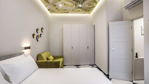 Quarto moderno com cama, poltrona verde, guarda-roupa e uma porta.