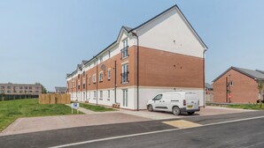 En fleretagers boligbygning med en facade i hvid og rød mursten, en parkeret varevogn og en klar himmel.