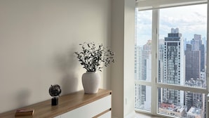 A modern room with a wooden cabinet, a potted plant, and a city view through large windows.