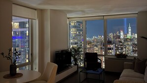 A modern living room with a city view, large windows, a flat-screen TV, and contemporary furniture.
