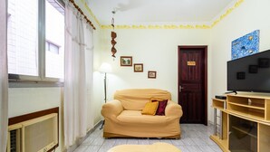 Una sala de estar con un sofá color crema, una mesita, un televisor y un radiador.