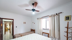 Un dormitorio con cama, ventilador de techo, ventana con cortinas y perchero.
