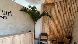 Ein Empfangsbereich mit Holzbude, einem Blumentopf, Korbschwinglampen, einer Sitzecke mit gewebtem Teppich und einer Wand mit vertikalen Holzleisten.