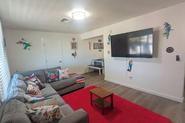 A living room with a grey sofa, red rug, and a flat-screen TV mounted on the wall. - 3-bedroom house in adorable Tucson with cool AC comfort-Casa la charrita (Tucson)