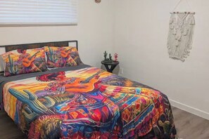 A bed with colorful bedding, a small side table with a cactus decoration, and a macrame wall hanging. - 3-bedroom house in adorable Tucson with cool AC comfort-Casa la charrita (Tucson)