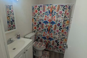 A bathroom with a white sink, toilet, and shower curtain with a floral pattern. - 3-bedroom house in adorable Tucson with cool AC comfort-Casa la charrita (Tucson)
