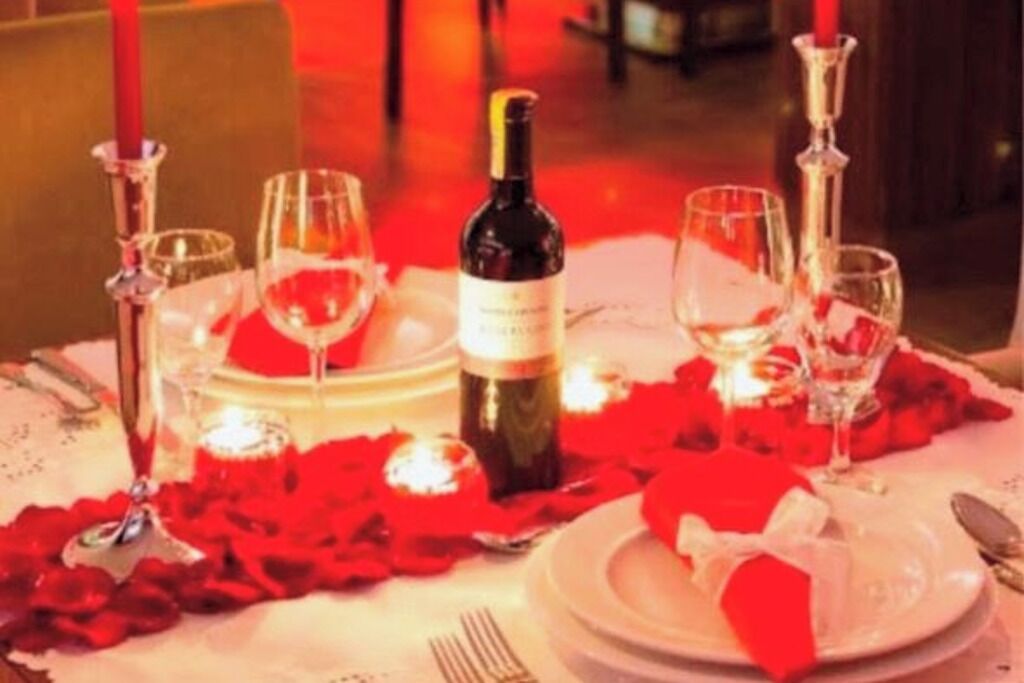 A table set for a romantic dinner with rose petals, candles, and wine glasses.