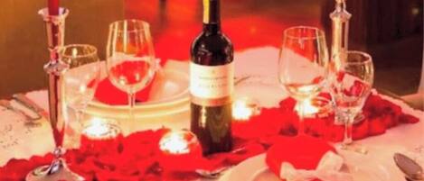 A table set for a romantic dinner with rose petals, candles, and wine glasses.