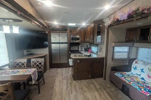 Cozinha compacta de RV com armários de madeira, geladeira, micro-ondas e pia.