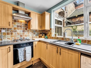 A modern kitchen with wooden cabinets, a tiled backsplash, a gas stove, and a window overlooking a brick building.