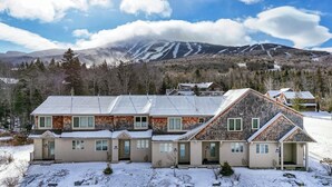 A multi-story building with a stone facade, multiple windows, and a snow-covered landscape with mountains in the background.