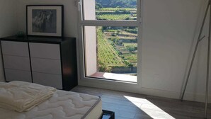 Un dormitori amb llit, un taulell i una finestra gran que ofereix vistes a un viñedo.
