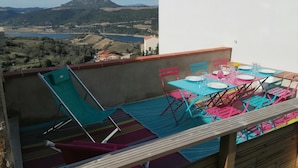 Un balcó amb taula preparada per dinar, cadires i vista a un llac i muntanyes.