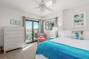 Ein Schlafzimmer mit Bett, Kommode, Sessel, Deckenventilator und einem Balkon mit Aussicht.