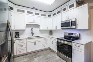 Una cocina moderna con armarios blancos, un refrigerador de acero inoxidable, un microondas, un horno y un lavavajillas.