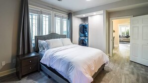 Ein Schlafzimmer mit einem Bett, einem Nachttisch, einer Waschmaschine und einer Tür zu einem anderen Raum.