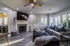 A spacious living room with a fireplace, a large flat-screen TV, a ceiling fan, and a sofa with patterned cushions. - Southern charm with a splash of modern decor (Savannah)