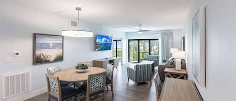 Un salon moderne avec un coin repas, de grandes fenêtres et un ventilateur de plafond.
