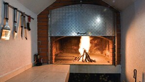 Uma lareira de tijolos com uma cobertura de metal, uma chama acesa no interior e um chão de azulejos.