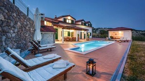 Uma villa moderna com piscina, área de estar ao ar livre e um muro de pedra.