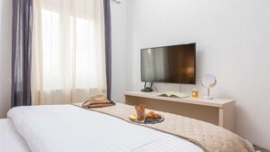 Quarto de hotel com cama, televisão, mesa de cabeceira com um livro, espelho e bandeja com petiscos.