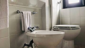 Ein Badezimmer mit zwei Toiletten, einem Waschbecken, einem Handtuchhalter und einem Fenster.