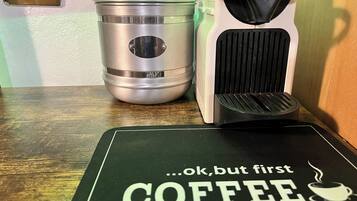Un piano di lavoro della cucina con una macchina da caffè, un contenitore in acciaio inossidabile e un sottopiattino verde con la scritta ‘…ok, ma prima CAFFÈ’.