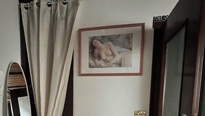 Una habitación con una silla blanca, un cuadro enmarcado en la pared, una puerta y un espejo.