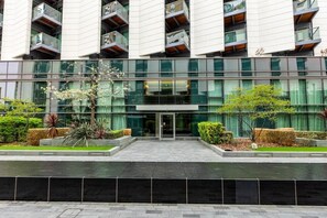 A modern building with a glass facade, multiple balconies, and a landscaped entrance area with plants. - Stylish Canary Wharf Flat & Balcony, 1 min to tube (Greater London)