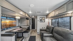 Interior compacto de um veículo recreativo, com cozinha compacta, área de estar e uma janela grande com vista.