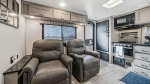 Cozinha compacta de motorhome com geladeira, micro-ondas, fogão e área de estar com dois reclináveis.