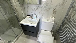 Uma casa de banho moderna com cabine de chuveiro em vidro, uma pia branca com armário preto, sanita e barra para toalhas.