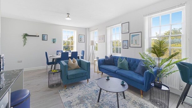 Uma sala de estar moderna com um sofá azul, uma área de jantar com cadeiras azuis e janelas amplas.