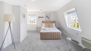 Quarto com cama, luminária, cadeira e janela.