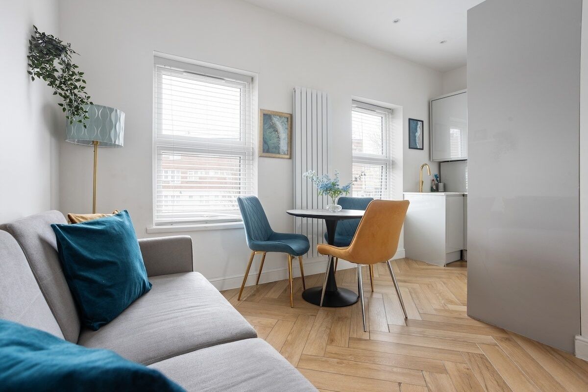 A modern living room with a grey sofa, blue chairs, and a small dining table.