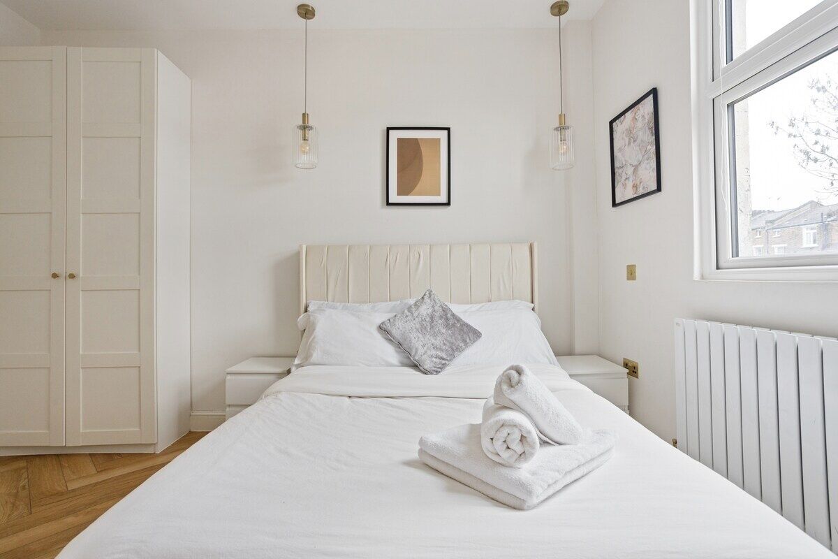A bedroom with a bed, white walls, a window, and a radiator.