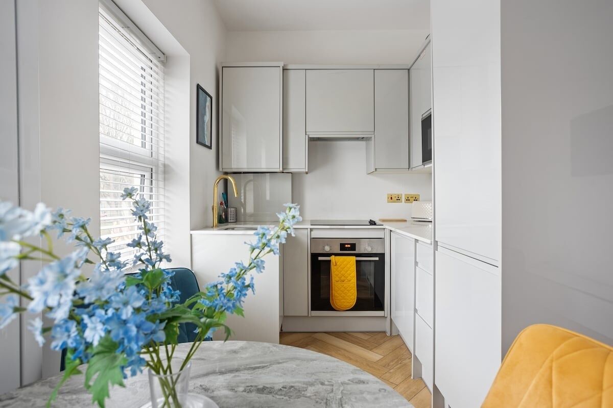 A modern kitchen with white cabinets, a built-in oven, and a yellow towel hanging on the oven handle.