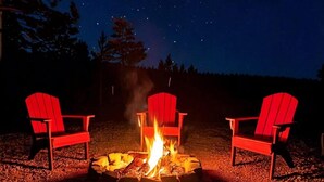A campfire with three red Adirondack chairs around it, set on a gravel surface under a starry night sky. - Joy Drive In Movie & RV Resort - Montana - Joy Drive In Movie & RV Resort - Montana (Copperas Cove)