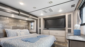 A bedroom with a bed, a TV, a window, and a small table with a tissue box. - Joy Drive In Movie & RV Resort - Montana - Joy Drive In Movie & RV Resort - Montana (Copperas Cove)