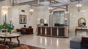 Eine Lobby mit Empfangsschalter, Sitzgelegenheiten, Kronleuchtern und einem großen Spiegel.