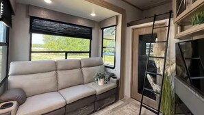 A modern interior with a beige sofa, a ladder, and a plant. - Joy Drive In Movie & RV Resort - 2bd Toy Hauler - Joy Drive In Movie & RV Resort - 2bd Toy Hauler (Copperas Cove)