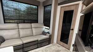 A compact living space with a sofa, a door, and a kitchenette. - Joy Drive In Movie & RV Resort - 2bd Toy Hauler - Joy Drive In Movie & RV Resort - 2bd Toy Hauler (Copperas Cove)