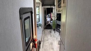 A narrow hallway with a kitchenette on the left, a small seating area in the center, and a closet with hanging clothes on the right. - Joy Drive In Movie & RV Resort - 2bd Toy Hauler - Joy Drive In Movie & RV Resort - 2bd Toy Hauler (Copperas Cove)