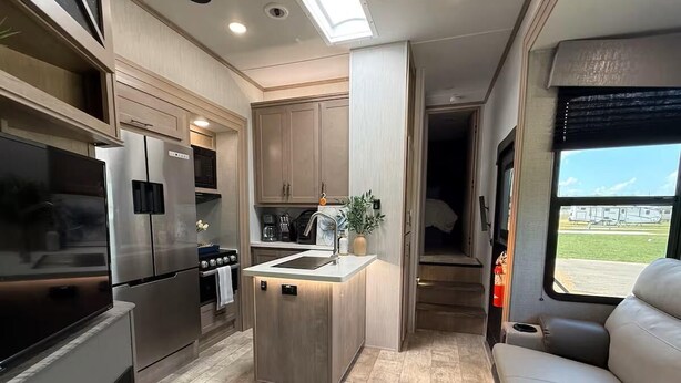 A compact kitchen with a central island, built-in appliances, and a seating area with a view. - Joy Drive In Movie & RV Resort - 2bd Toy Hauler - Joy Drive In Movie & RV Resort - 2bd Toy Hauler (Copperas Cove)