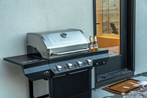 Ein schwarzer Grill für den Außenbereich mit vier Kochfeldern und einem digitalen Display, vor einer hellen Wand platziert.